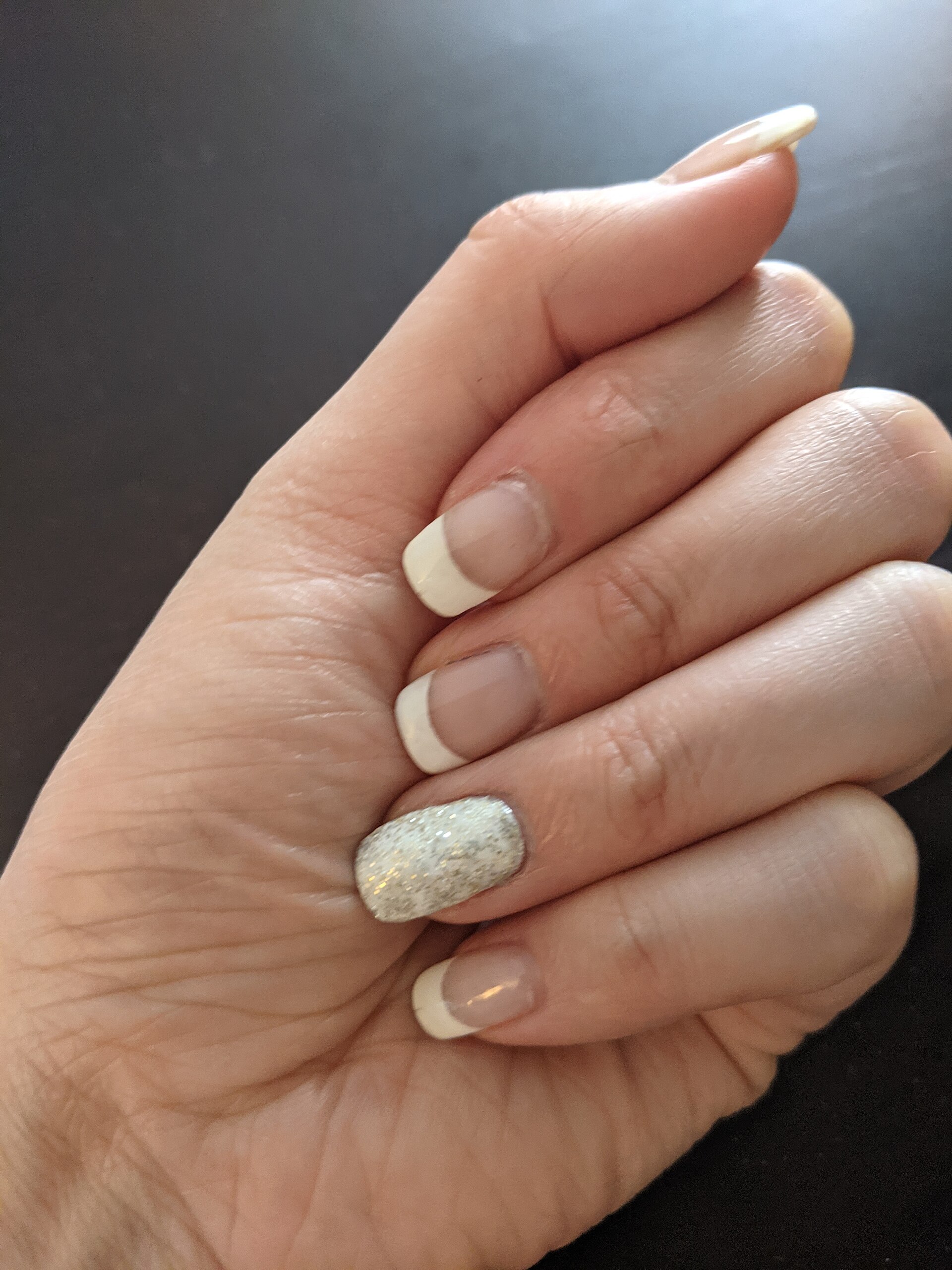 Detalle de una manicura francesa con pedrería y brillo en el dedo anular.