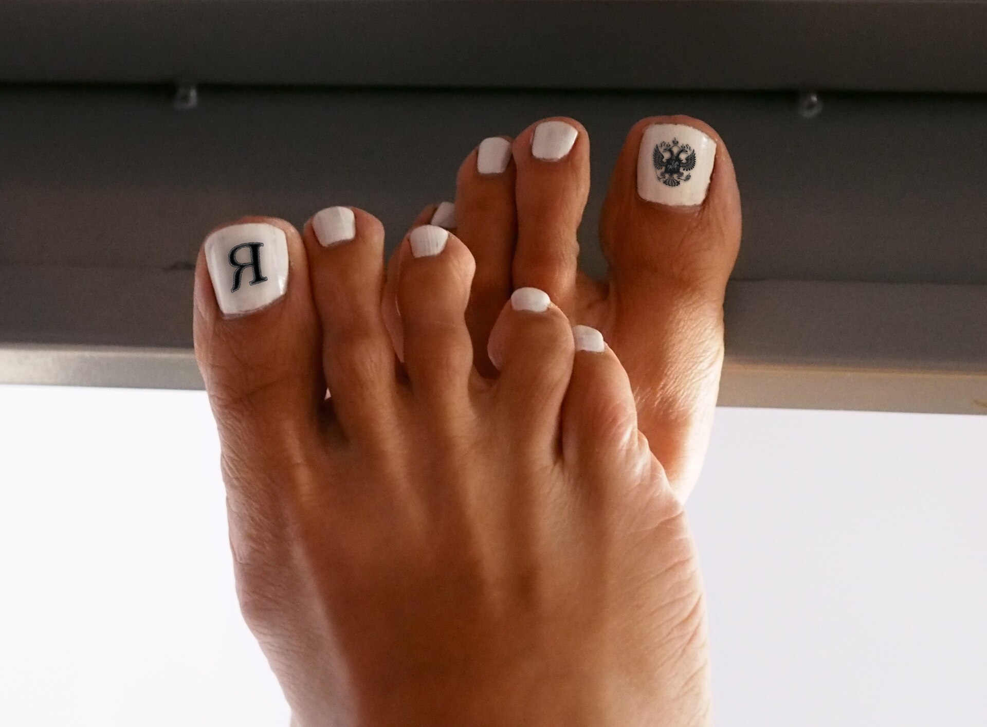 Manicurista aplicando esmalte rojo sobre las uñas de una clienta, visto en primer plano.